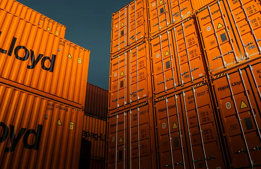 Orange shipping containers stacked high against a dark sky in the container yard