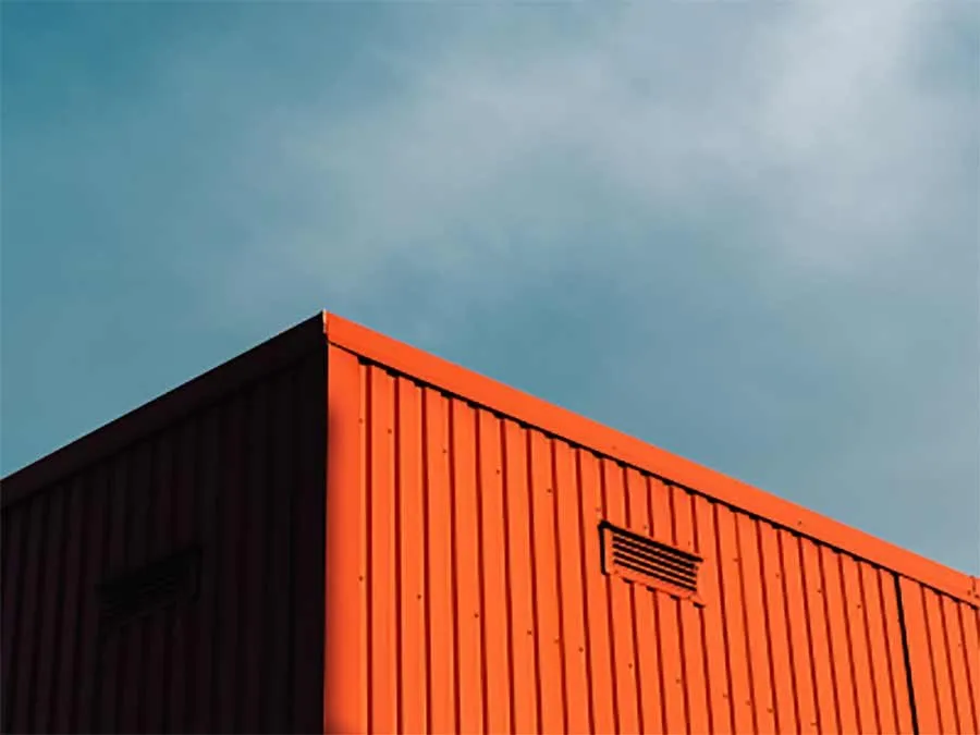 Corner of a freshly painted orange shipping container against a blue sky