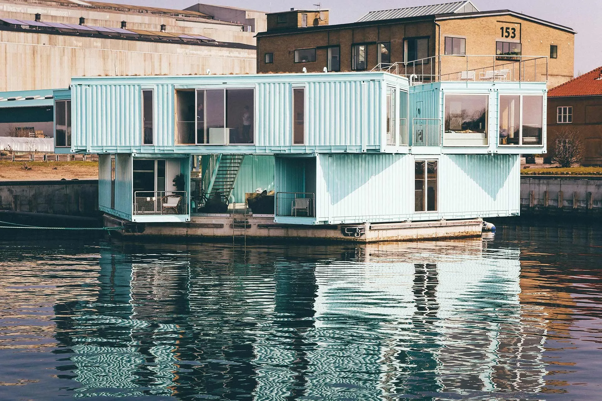 Relocatable container buildings with full-height glazing, stacked two storeys at the water's edge